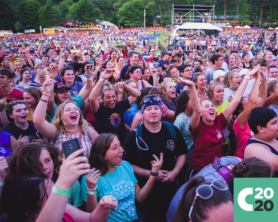 A crowd of young people at an outdoor Christian music festival. Some people have their arms raised in praise.